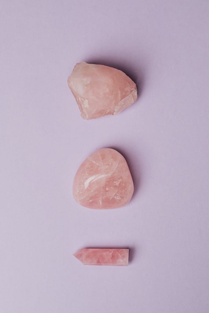 A minimalist composition of three rose quartz stones on a soft purple background, showcasing their natural beauty.