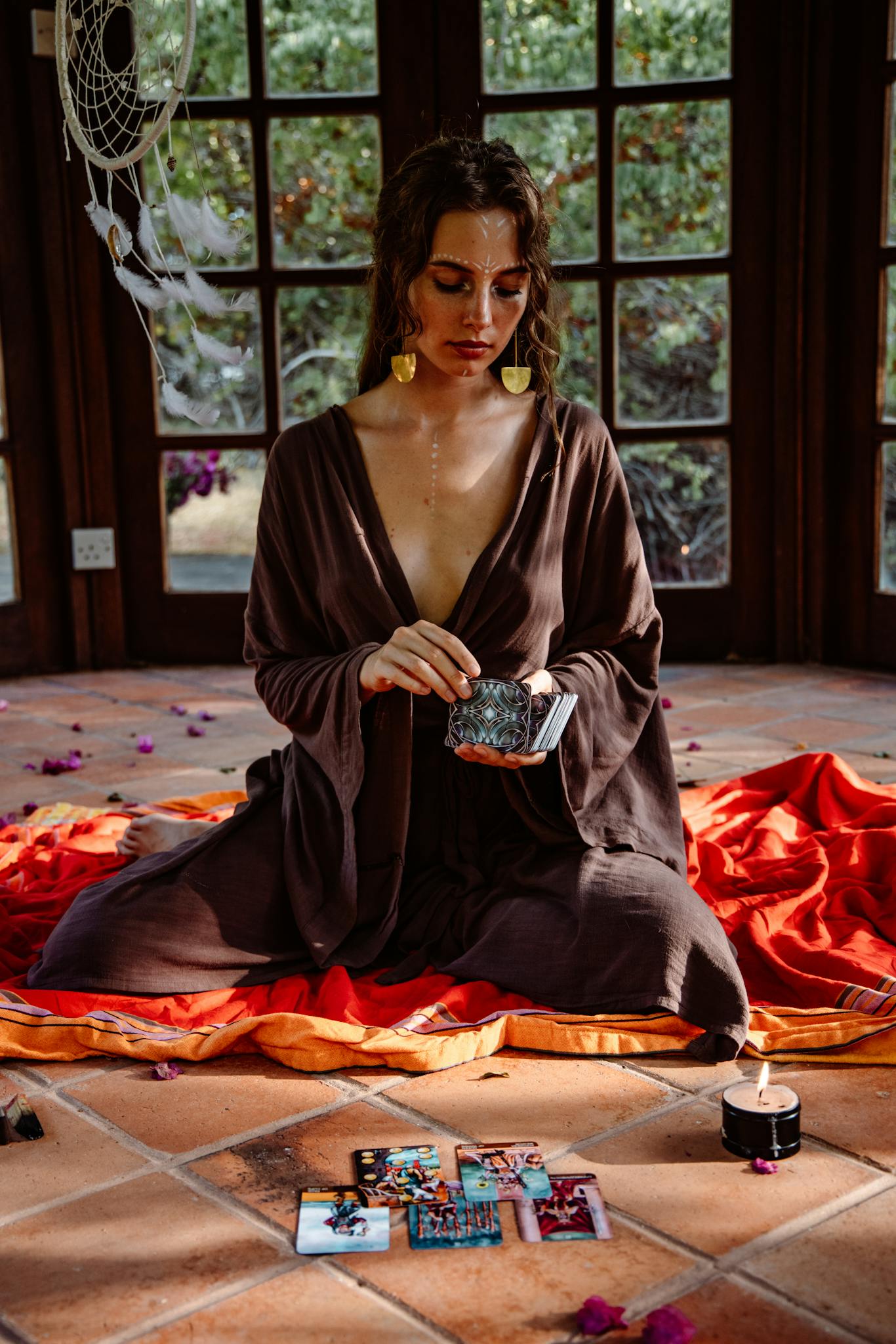 A woman sitting indoors, performing tarot readings with candles and a dreamcatcher.