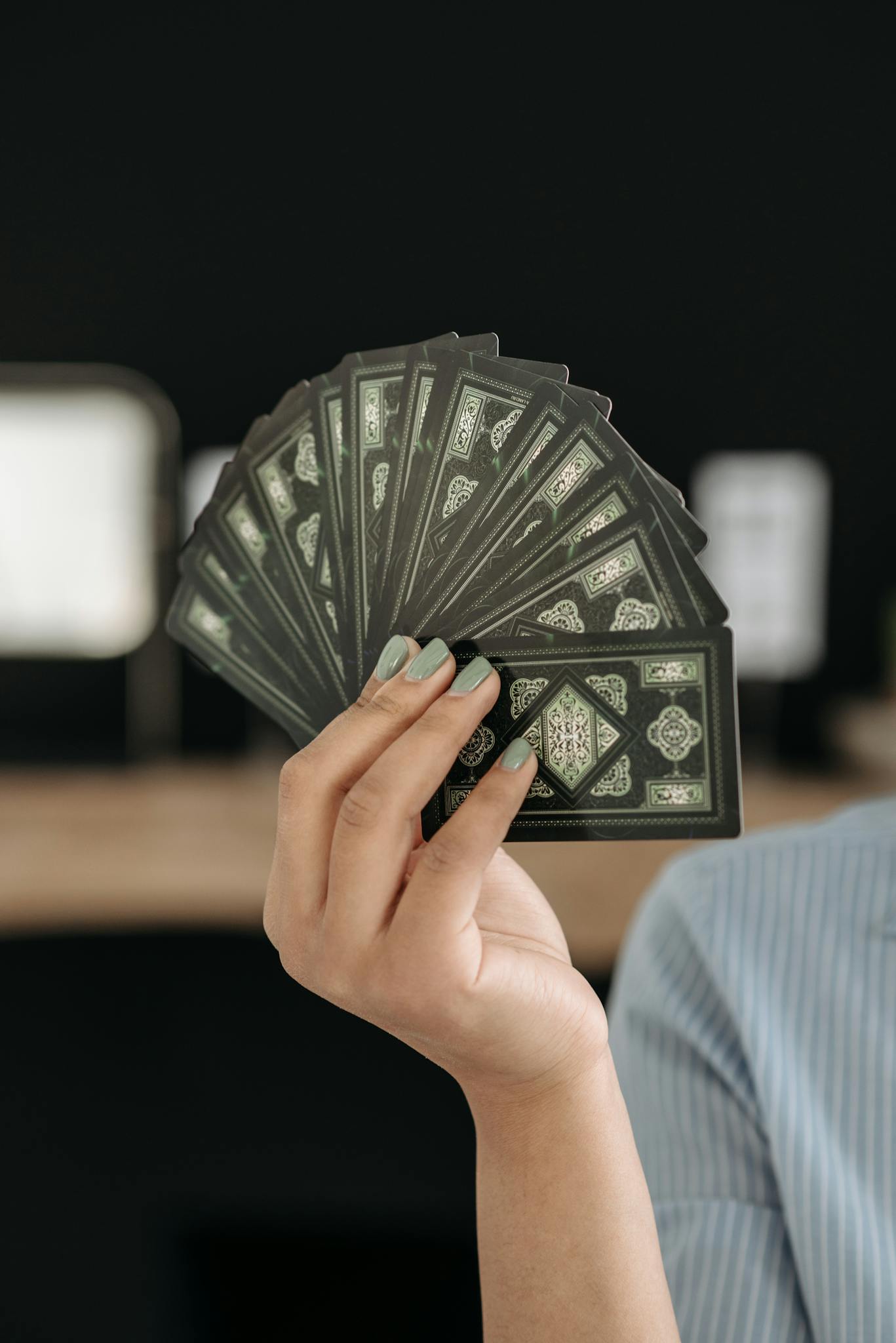 A woman's hand elegantly holds a fan of tarot cards against a blurred background.