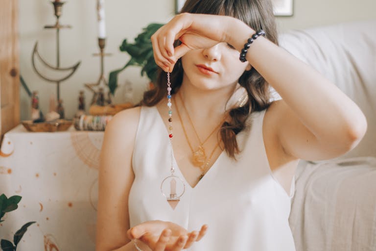 A young woman uses a pendulum for divination in a serene, indoor setting.