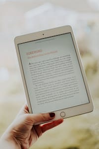 Close-up of a hand holding a tablet displaying an e-book page.