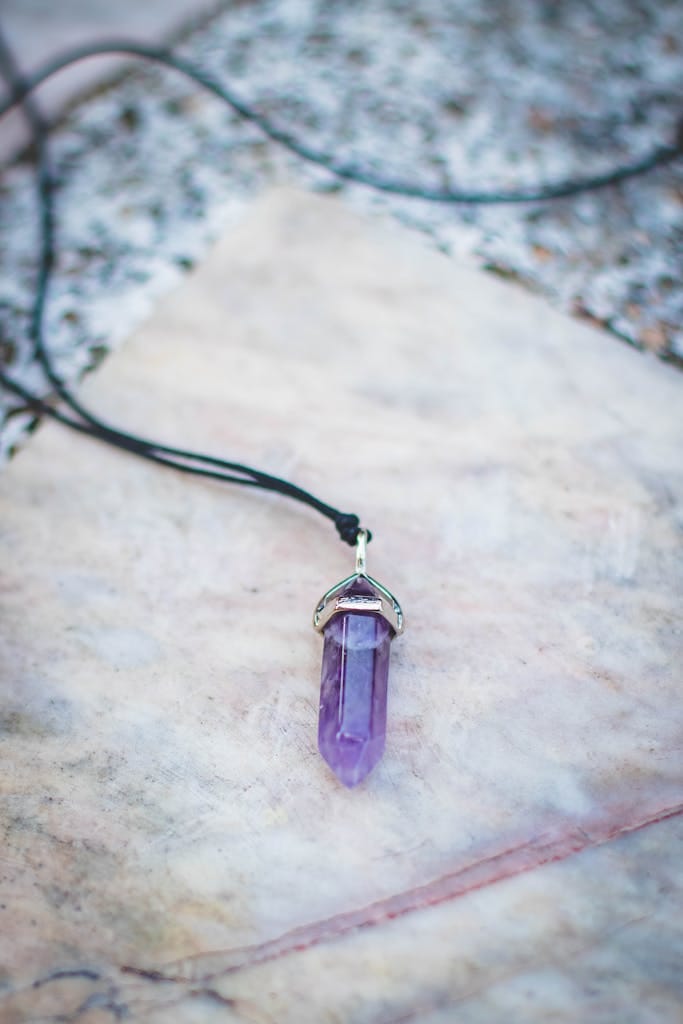 Close-up of a purple amethyst pendant necklace on marble background.