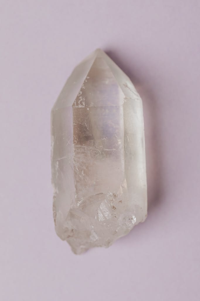 Minimalist photo of a natural clear quartz crystal isolated on a light pastel background.