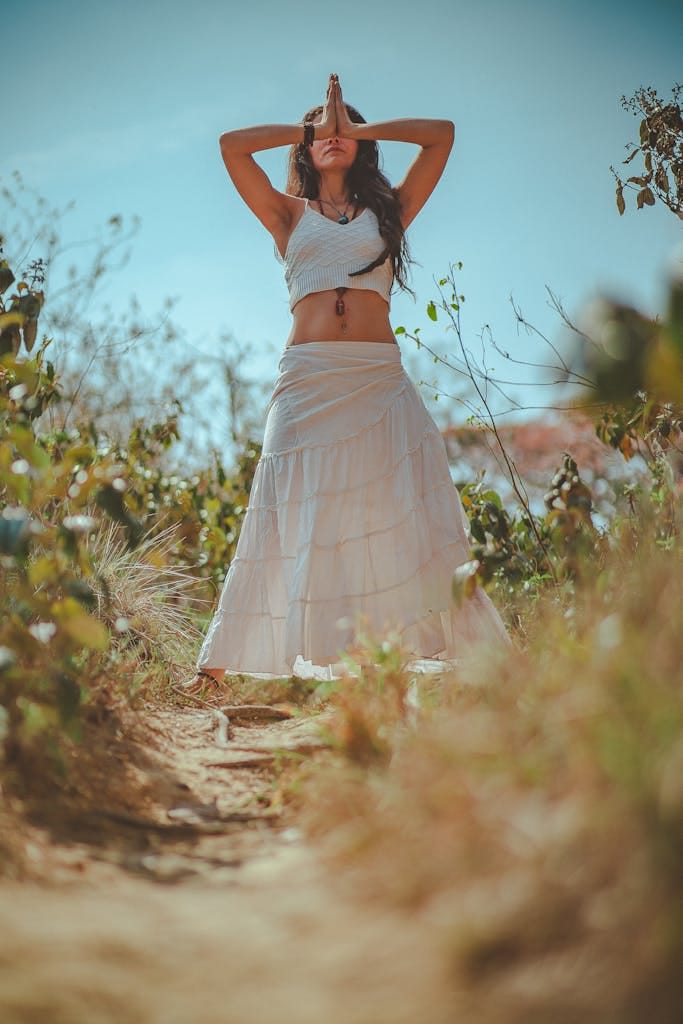 Young woman meditating in a peaceful outdoor setting wearing a white skirt.